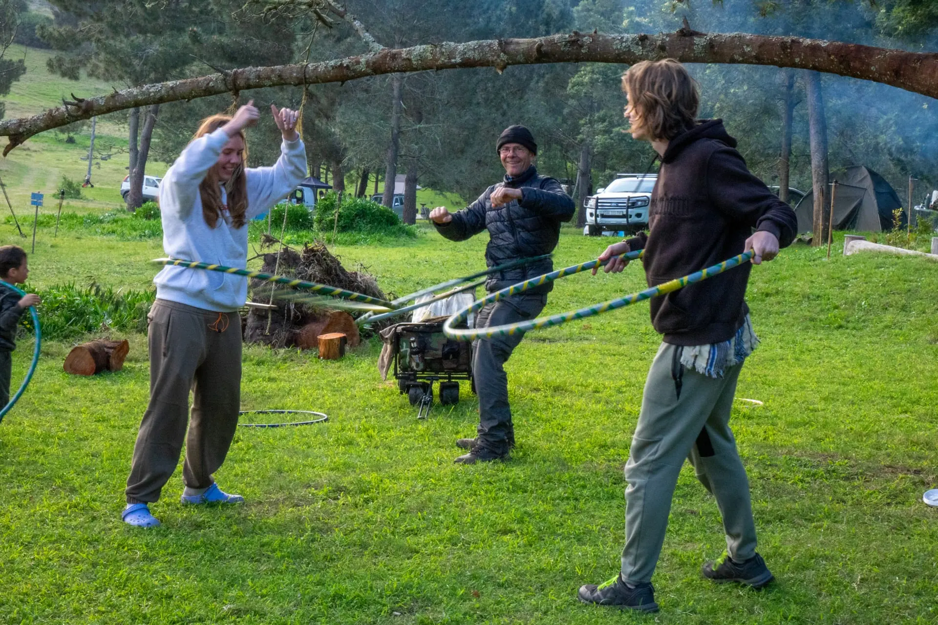 Three friends hula hoop together beneath a tree at the campsite