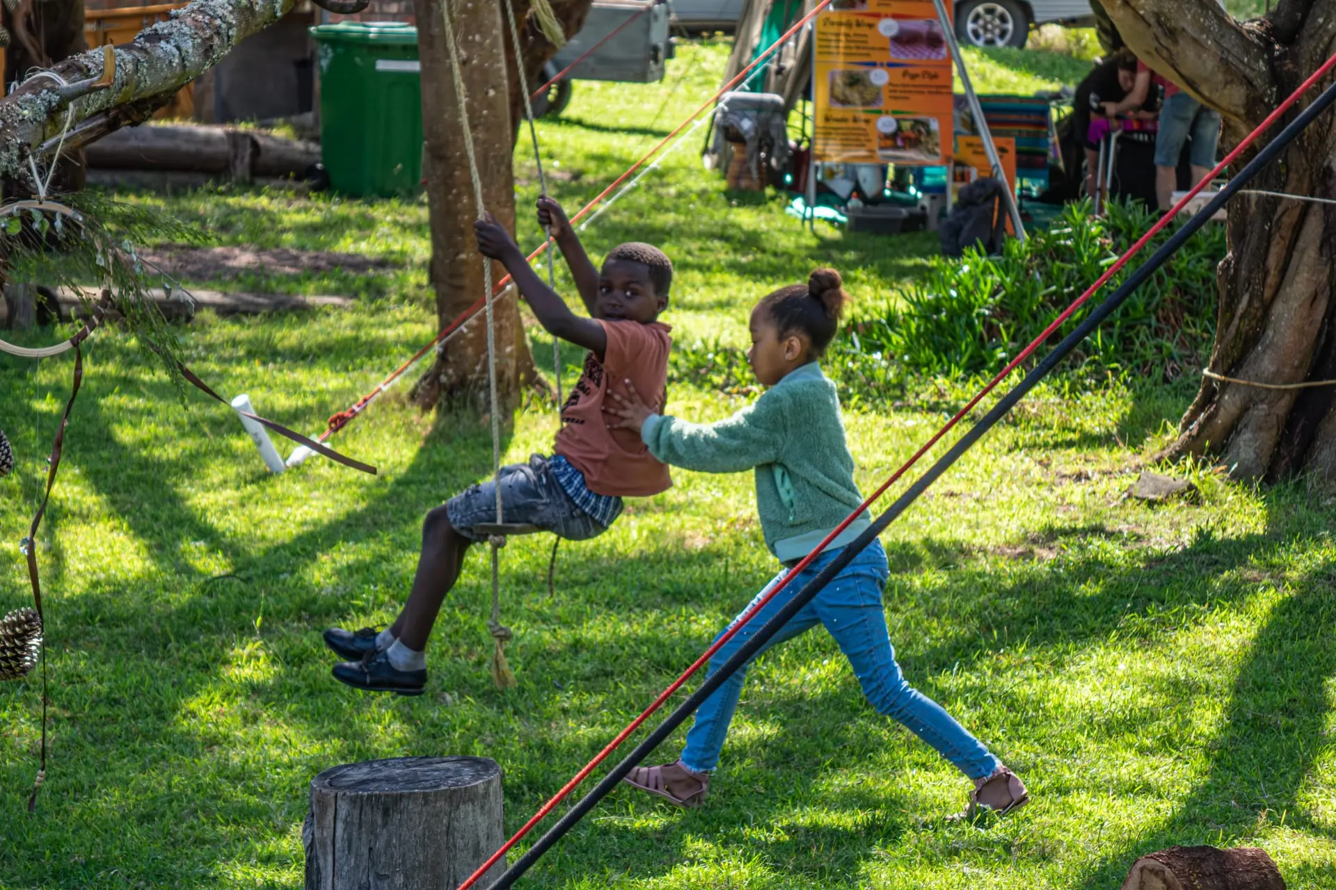 Two children play on a rope swing beneath the trees at Well-Being Sanctuary
