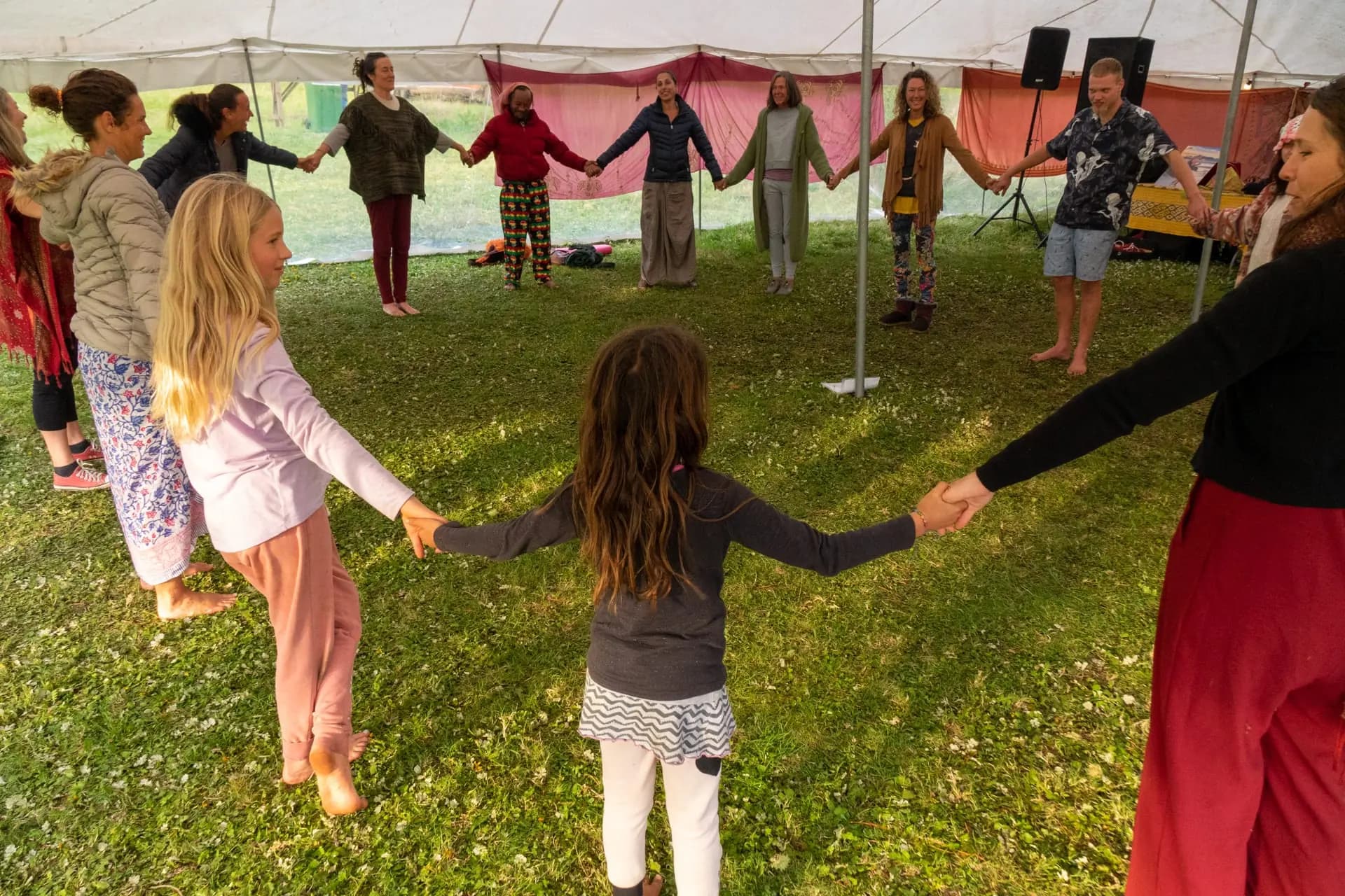 A large circle of people holding hands together under a festival tent