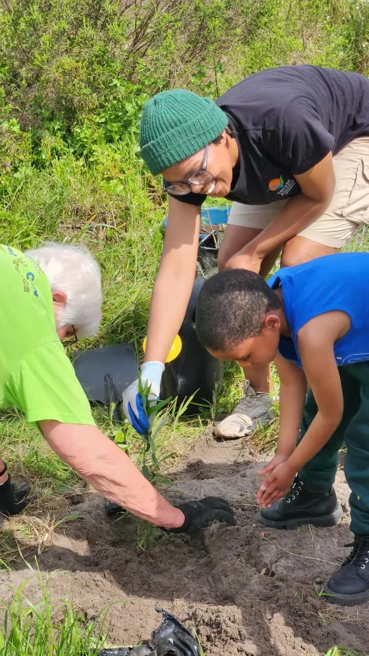 Three generations kneeling together to firm the soil around a newly planted sapling