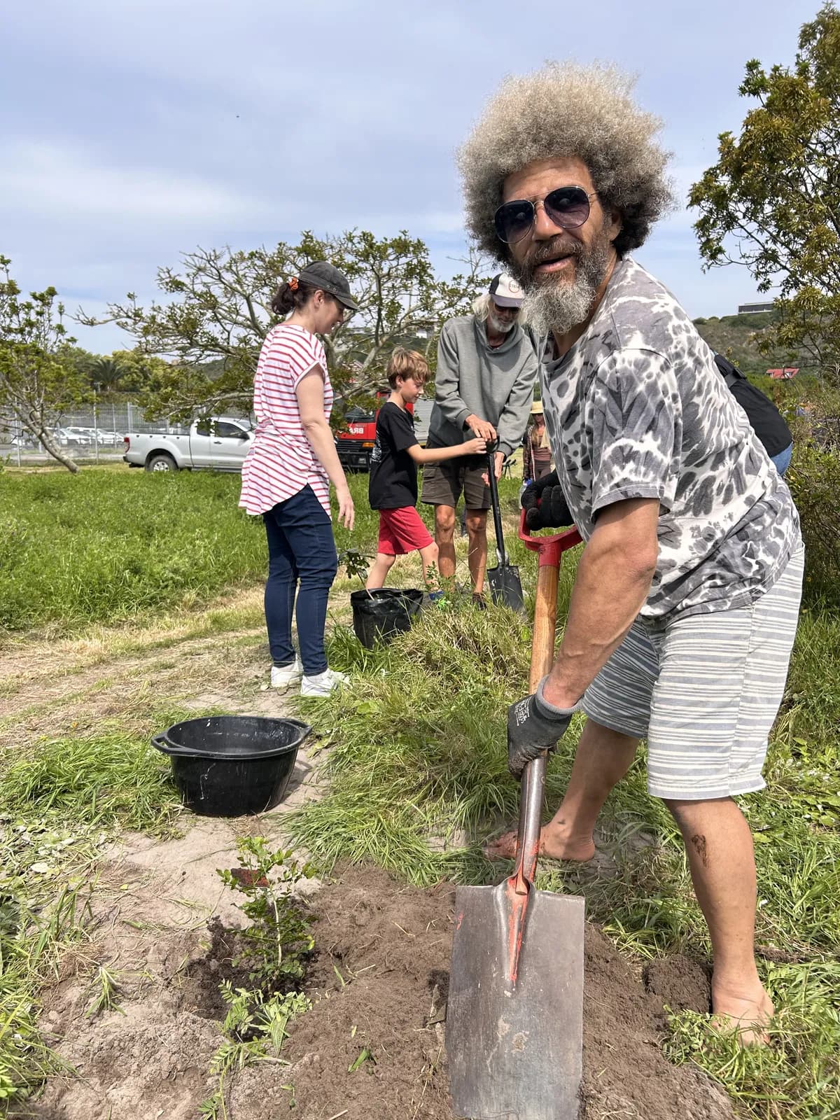 A volunteer leaning on his spade beside a newly dug planting hole