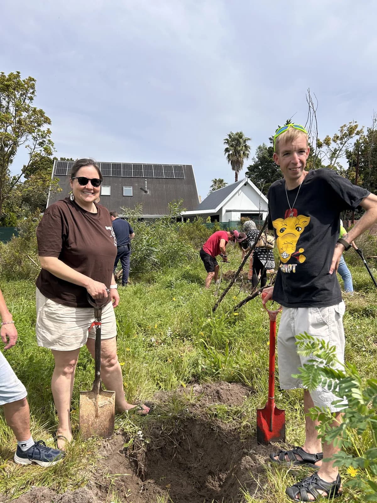 Two volunteers pausing with their spades beside a freshly dug planting hole